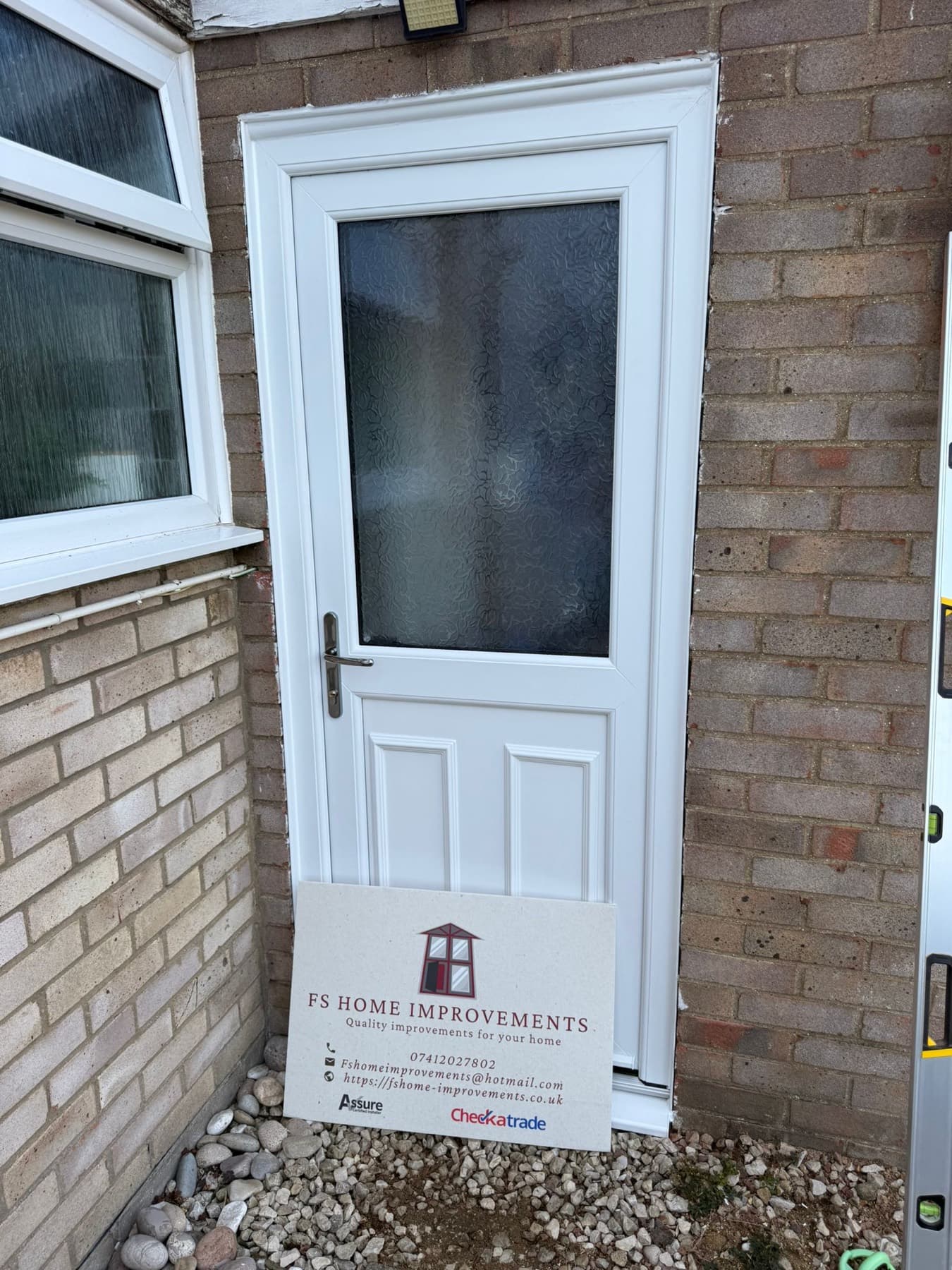 White half-glazed uPVC side door with obscure patterned glass, twin raised lower panels and chrome handle in a brick side passage